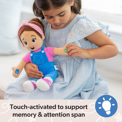 Girl in blue dress holds an interactive plush doll in pink and blue overalls, touching a green sensor on its arm