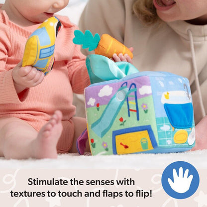 Baby and adult playing with a soft sensory activity cube showing a playground & bathroom, plus plush bus & carrot toys
