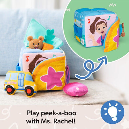 Soft Ms. Rachel peek-a-boo activity cube featuring Ms. Rachel's face, a teddy bear, a school bus toy, colorful stars, and music notes