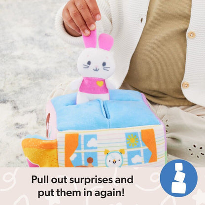 Child's hand pulls a white plush bunny with pink ears and shirt from a vibrant soft toy house featuring windows and a sun design