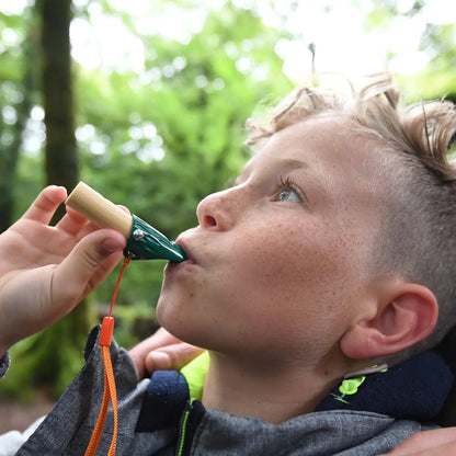 Boy blowing into a green and wooden bird call or whistle outdoors