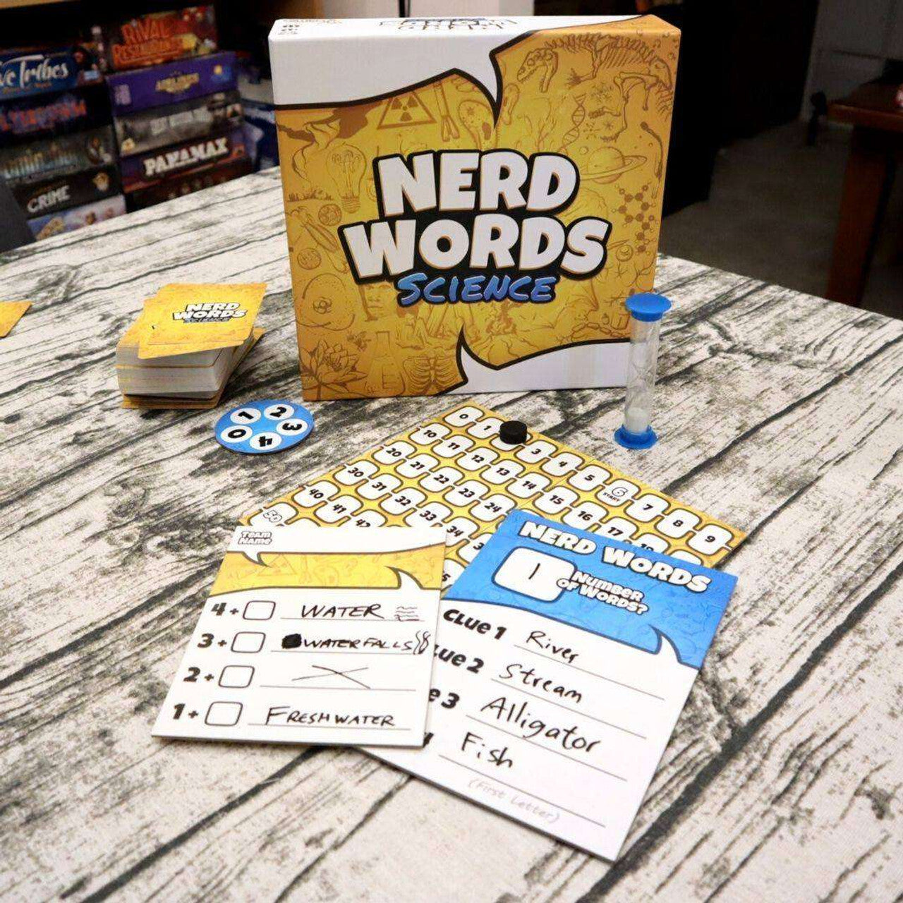 Nerd Words Science board game components, including cards, hourglass, and score sheets, spread on a wooden table