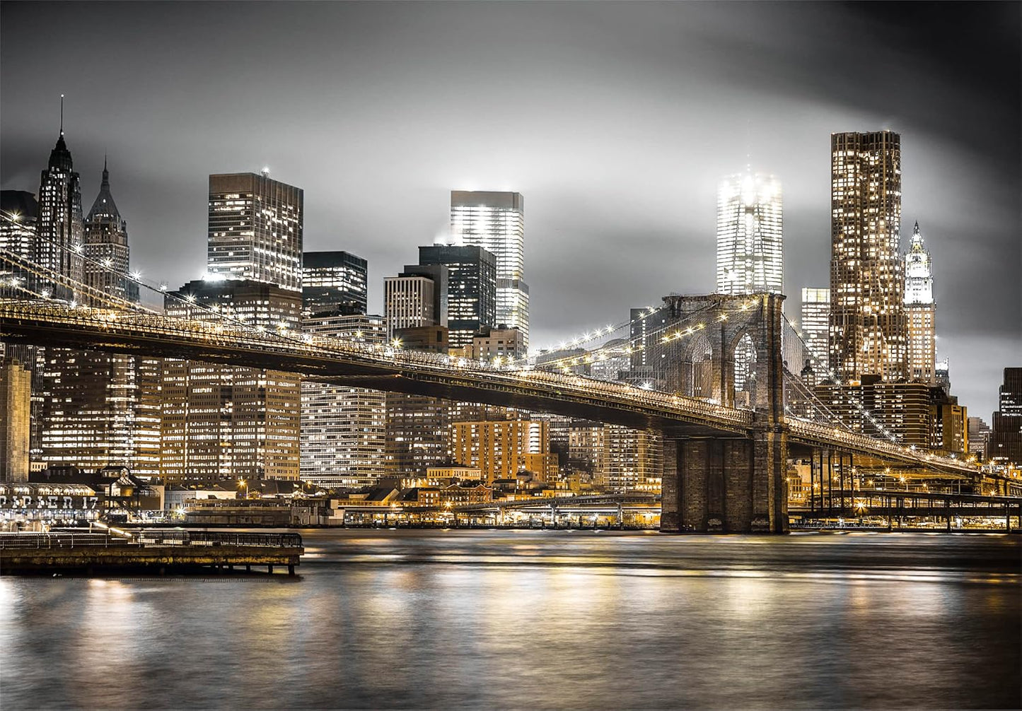 Illuminated Brooklyn Bridge at night, with golden city lights reflecting on the water