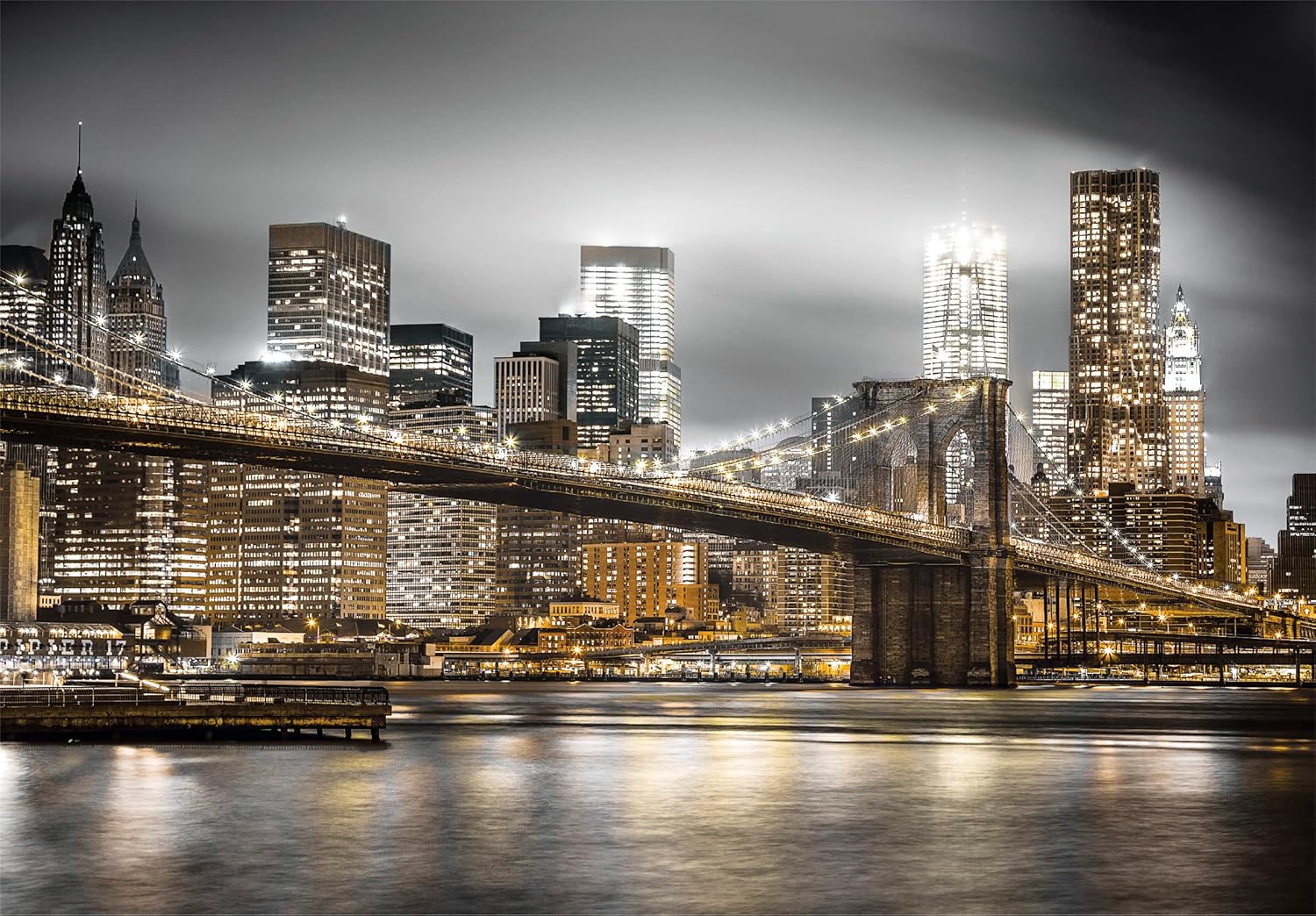 Illuminated Brooklyn Bridge at night, with golden city lights reflecting on the water