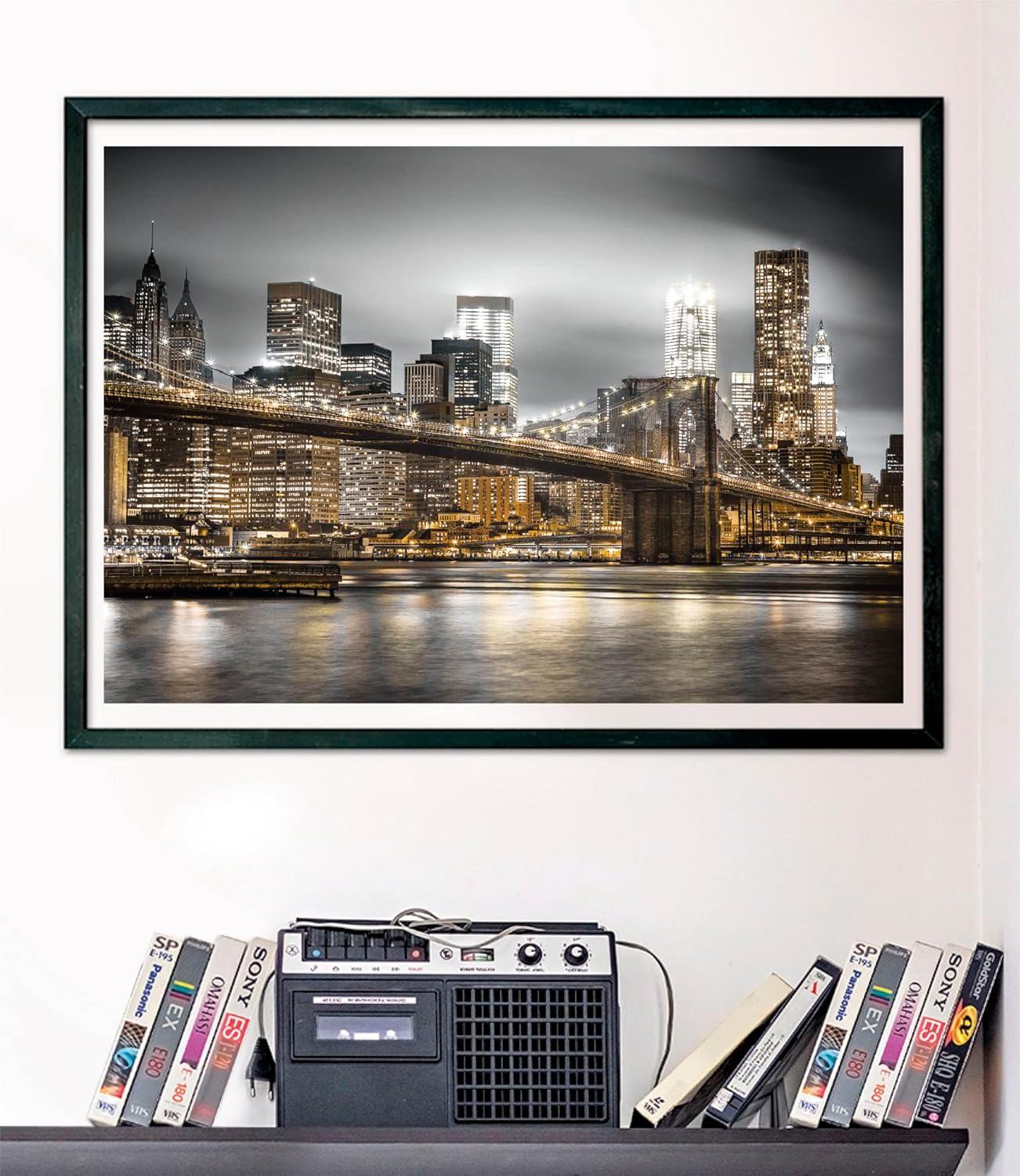 Framed black and white photo of Brooklyn Bridge & illuminated NYC skyline at night, golden lights reflecting on water