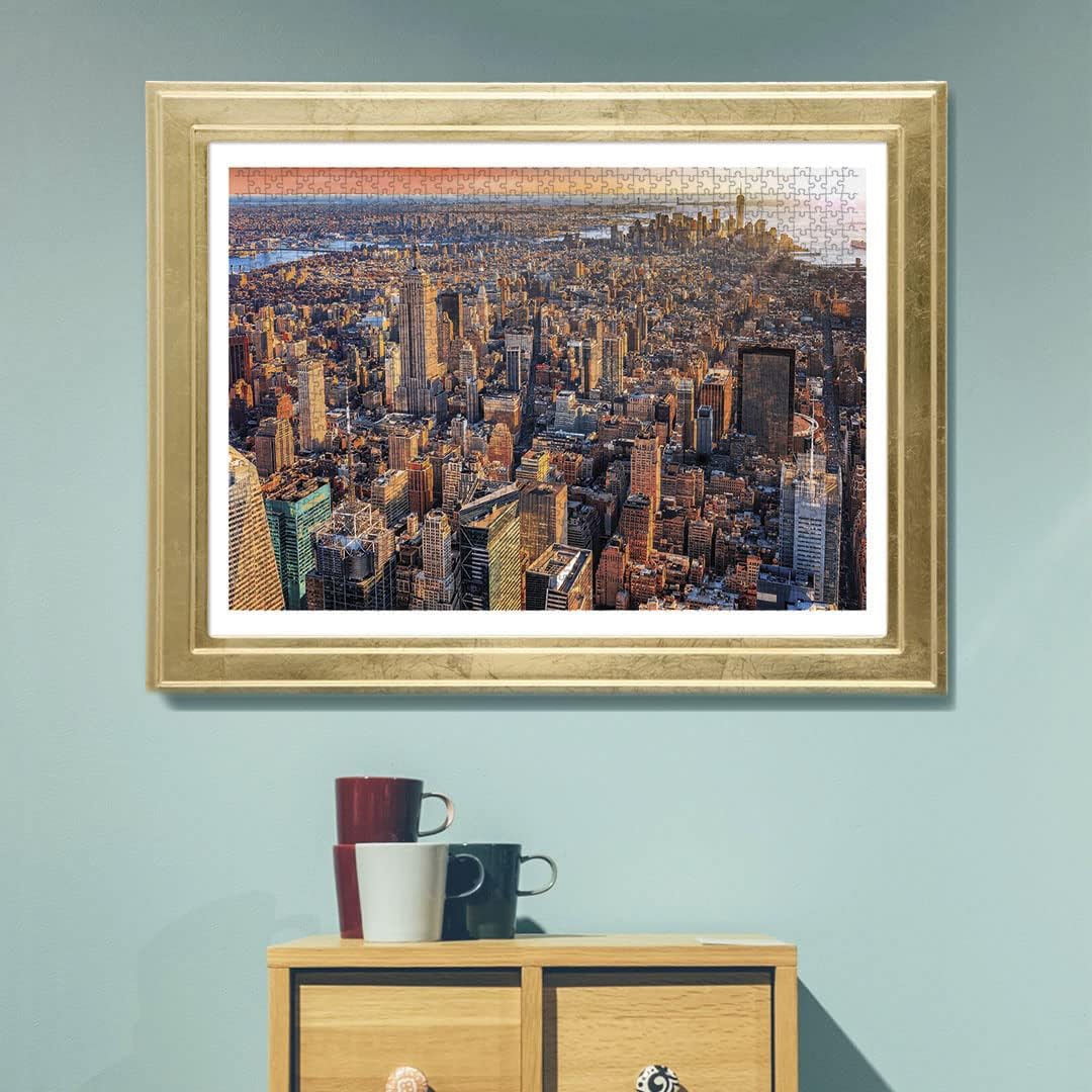 A framed jigsaw puzzle depicting an aerial view of New York City's skyscrapers, with visible pieces, on a blue wall.