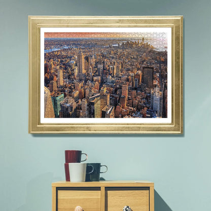 A framed jigsaw puzzle depicting an aerial view of New York City's skyscrapers, with visible pieces, on a blue wall.