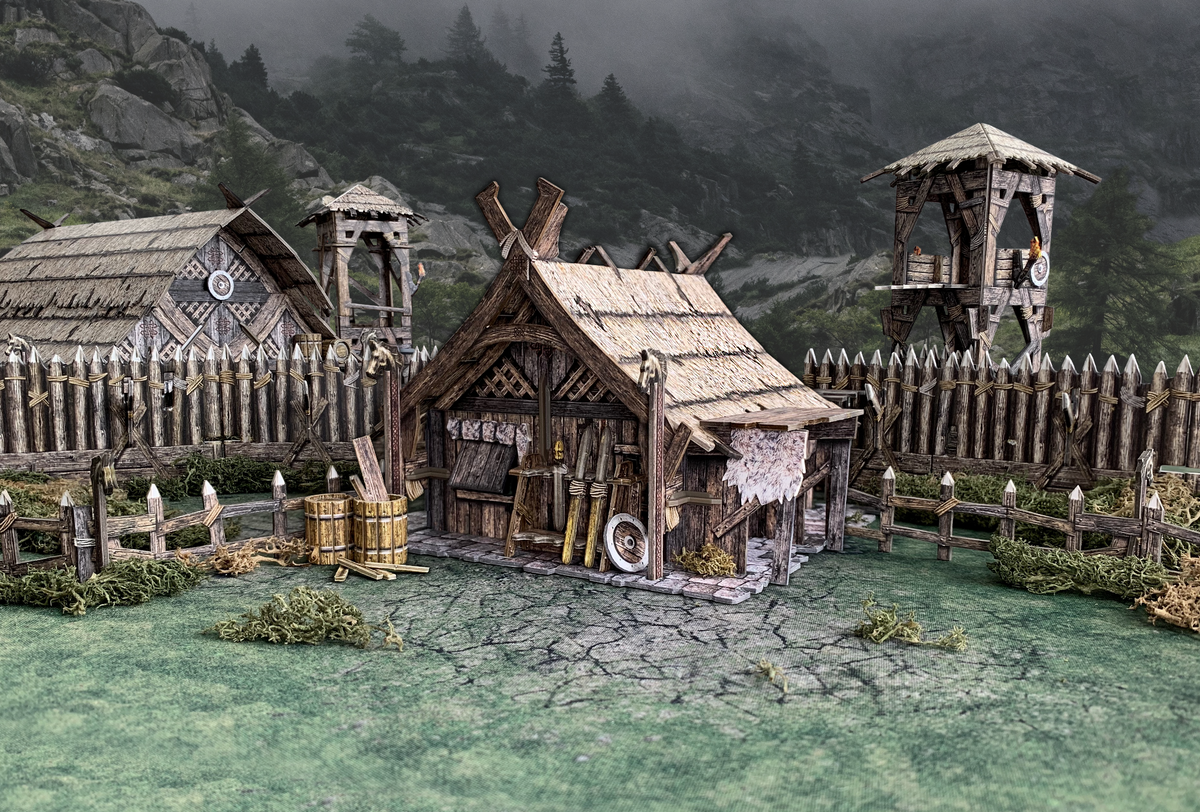 A diorama of a fortified Viking village with thatched huts, watchtowers, and palisade fences set against misty mountains.