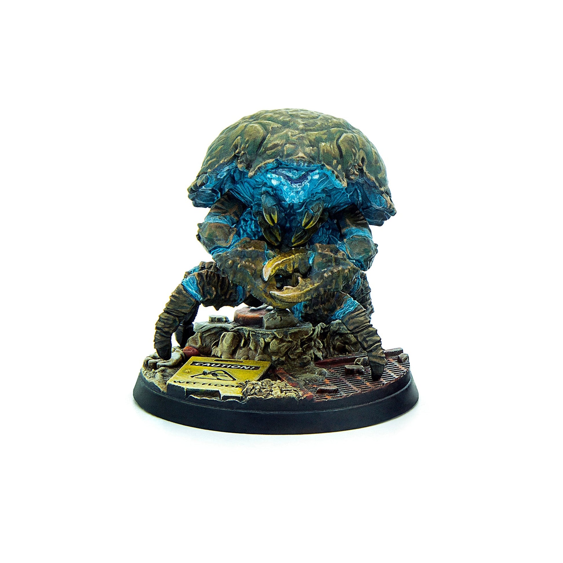 A detailed miniature of a blue and brown crab-like alien with glowing face and large claws, on a base with a "CAUTION!" sign