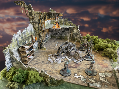 Battle Systems Crypts and Caverns Dungeon Upgrade Pack showcasing ruins a wooden bookshelf an ancient siege weapon and various fantasy miniatures on a detailed battlefield terrain