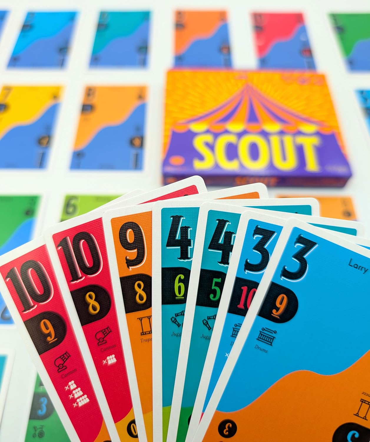 A fan of colorful "Scout" game cards showing numbers and circus icons, with the game box blurred in the background