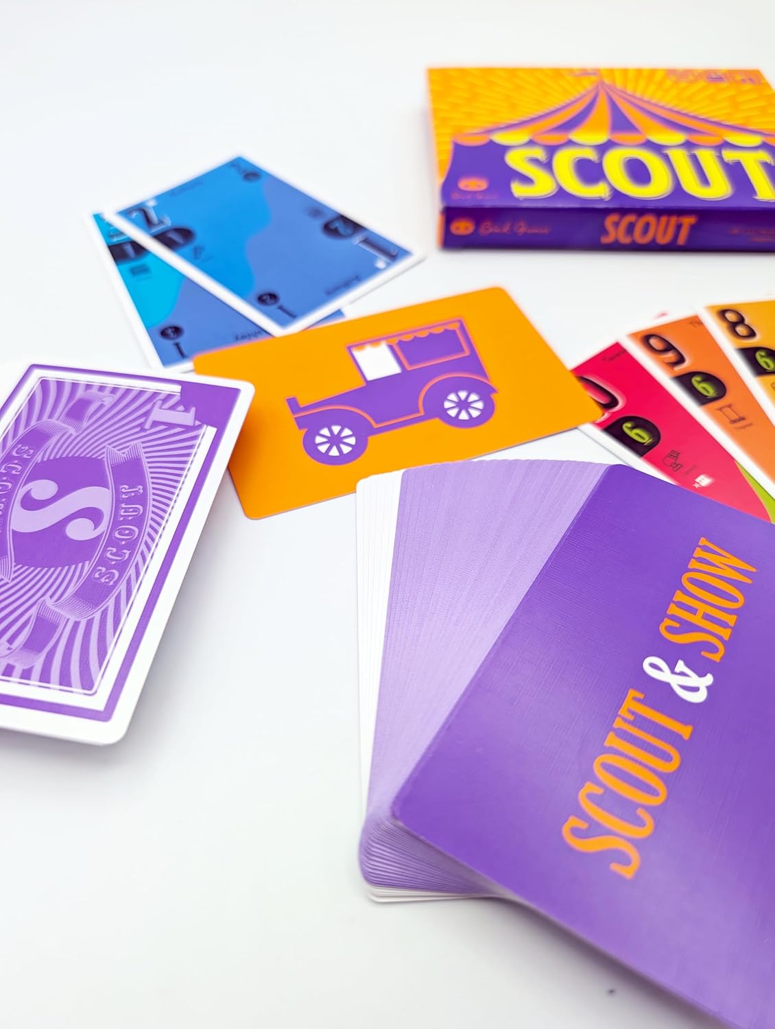 Scout board game components: box, colorful cards with numbers and designs like a purple vintage car, on white