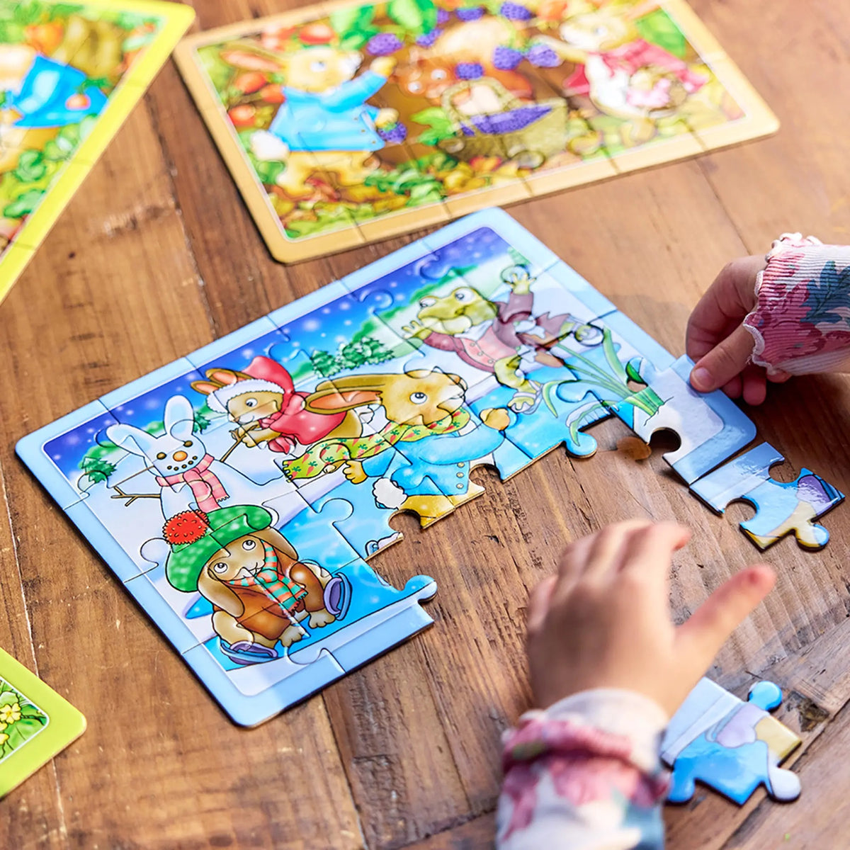 Child&#39;s hands assembling a winter-themed puzzle featuring cartoon rabbits and a snowman
