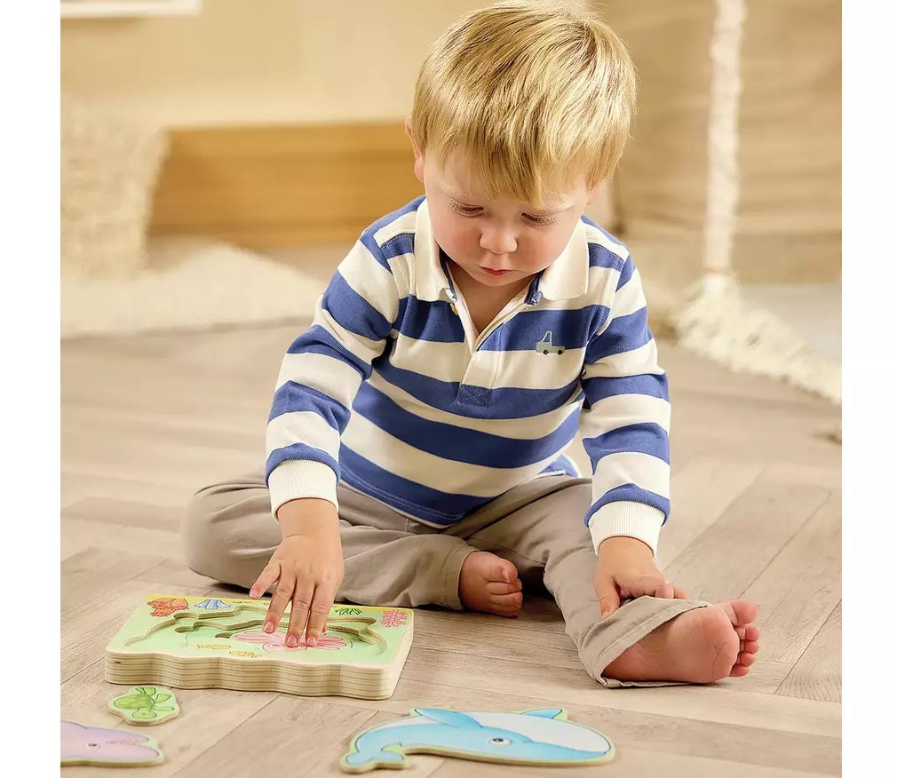 Blonde toddler in striped shirt plays with a wooden animal shape puzzle on the floor