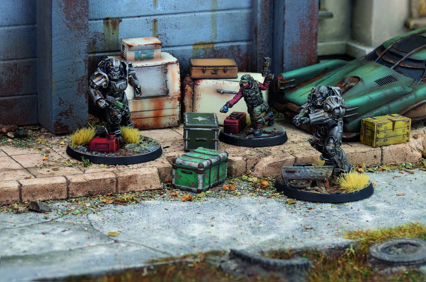 Three sci-fi miniatures: two power-armored, one tactical human, scavenging amidst debris, crates, and a rusted car
