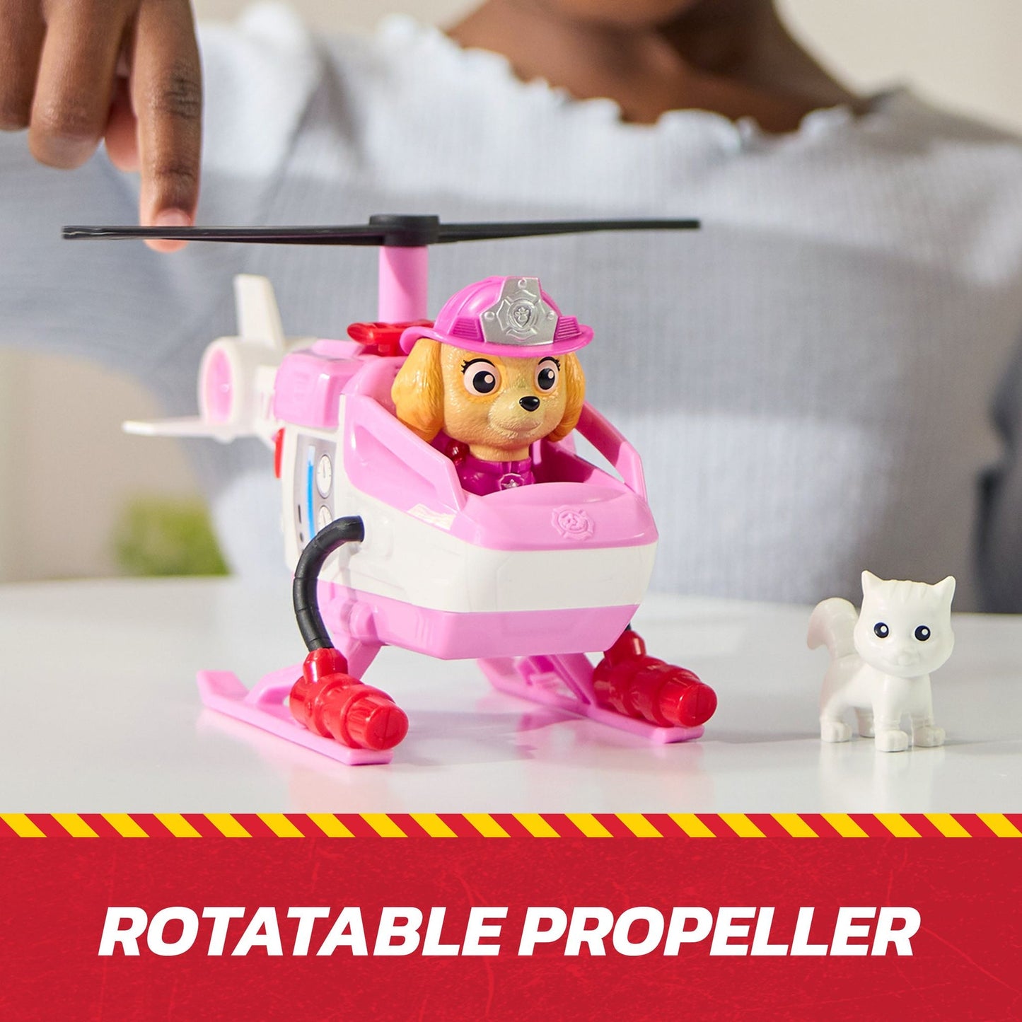Skye from Paw Patrol in a pink and white toy helicopter, a child's finger touching its rotatable propeller