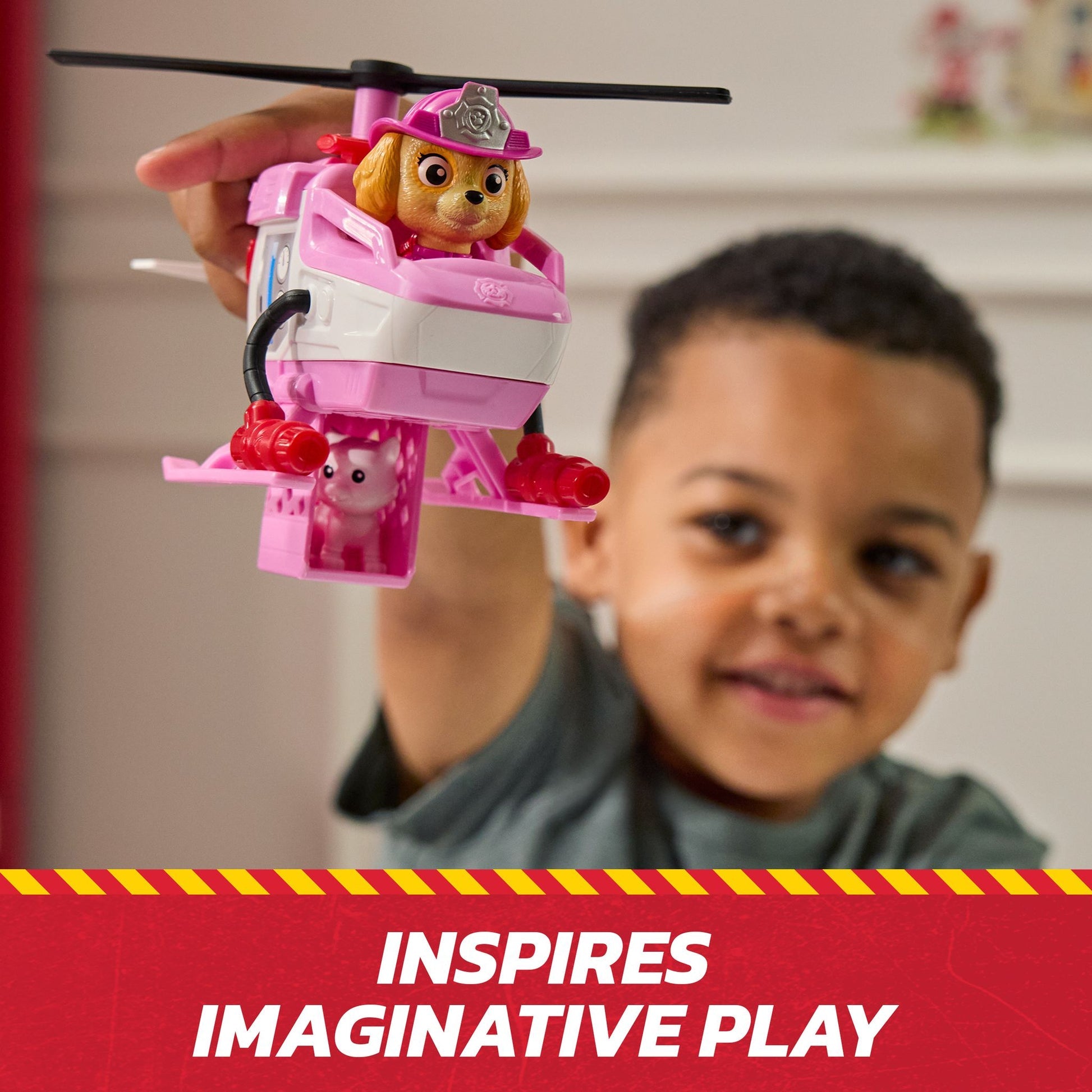 Child holds a pink Paw Patrol Skye helicopter toy with a dog figure and a small pig in a rescue cage