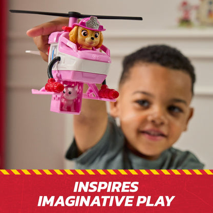 Child holds a pink Paw Patrol Skye helicopter toy with a dog figure and a small pig in a rescue cage
