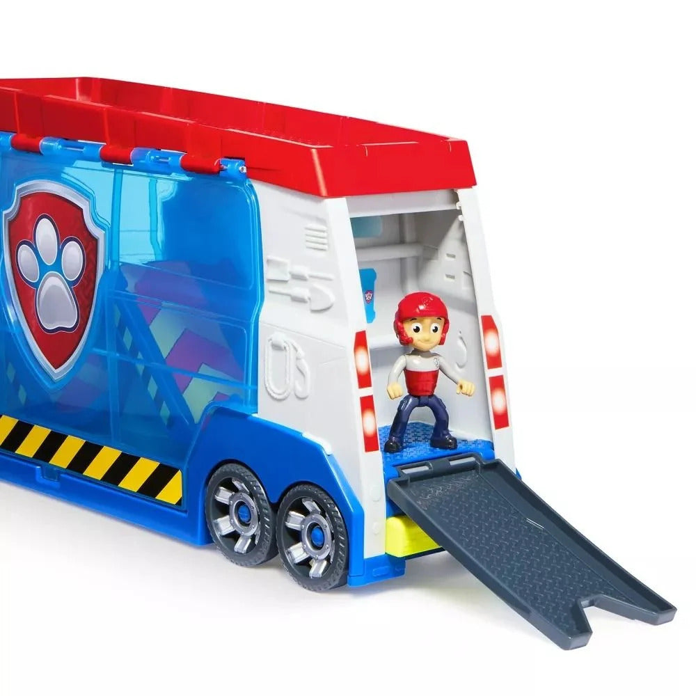 Red, white, and blue Paw Patrol toy truck with Ryder figure on its extended rear ramp, features a paw print logo and yellow hazard stripes