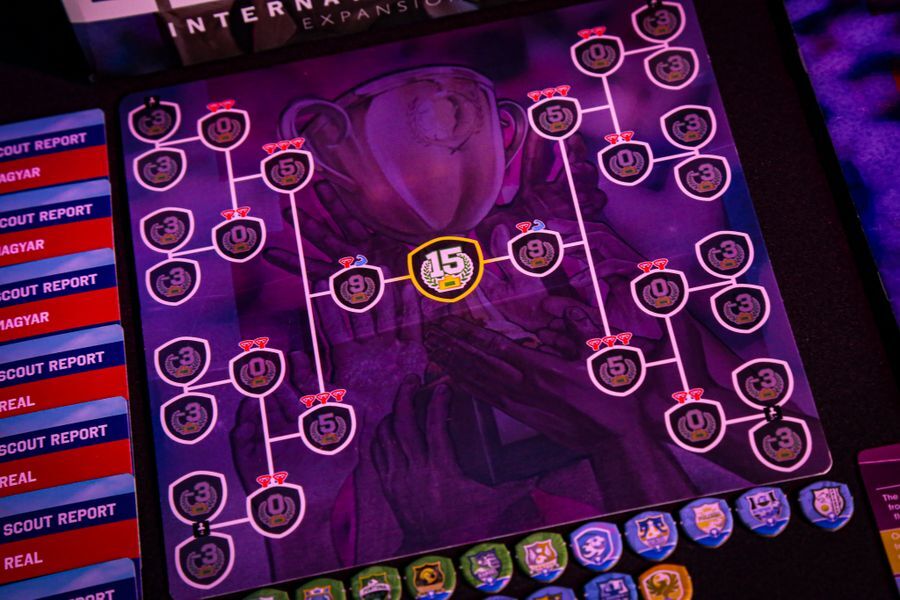 Close-up of a board game showing a tournament bracket with colorful game pieces on a dark surface