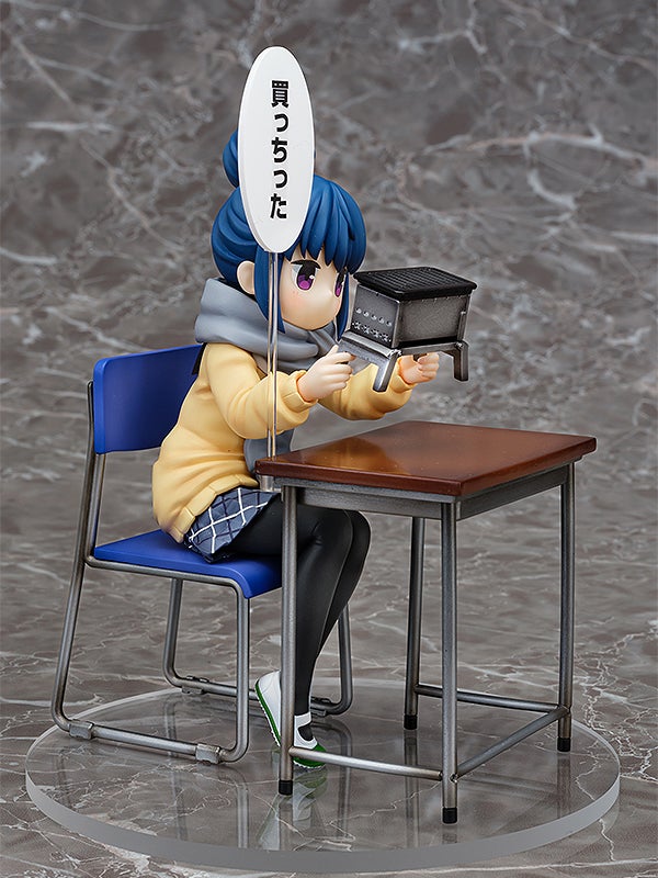 Anime figure of a girl sitting at a school desk holding a miniature barbecue grill with a speech bubble saying I bought it
