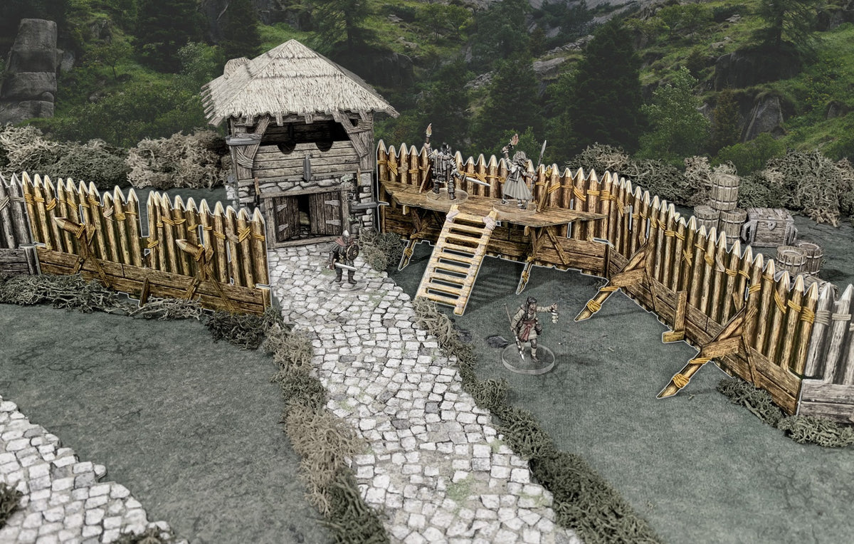 A tabletop game: A fortified wooden outpost with a thatched building and palisade, featuring miniature warriors and adventurers on a path.