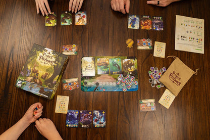 Hands around a wooden table playing the Parks & Potions board game with its box, cards, tokens, game board, and rulebook spread out