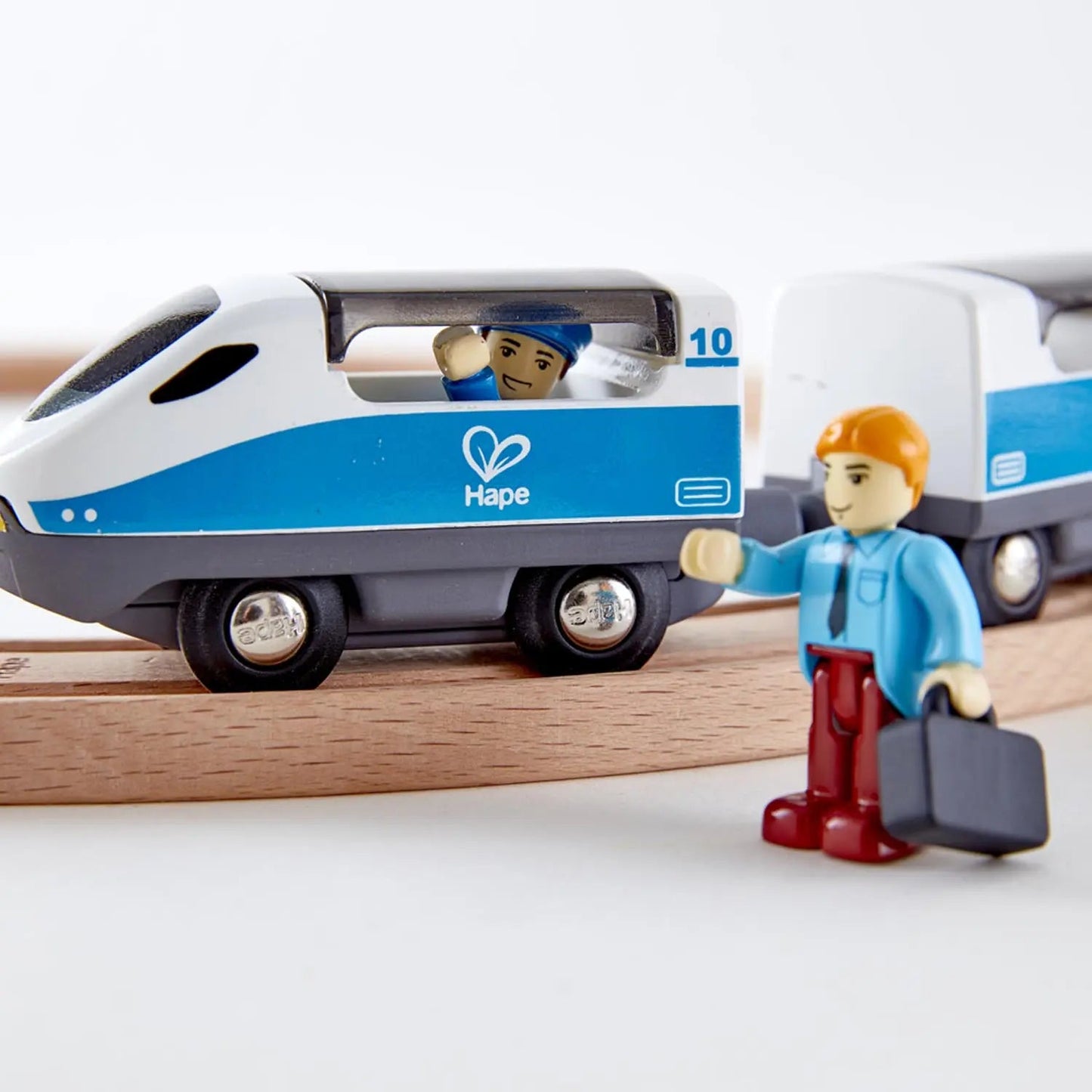 Toy train engine on wooden tracks with a driver waving to a figure holding a briefcase