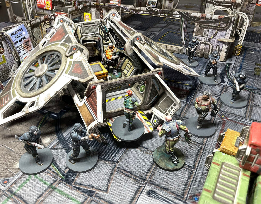 Sci-fi tabletop game with armed miniatures surrounding an opened futuristic dropship on a detailed urban board