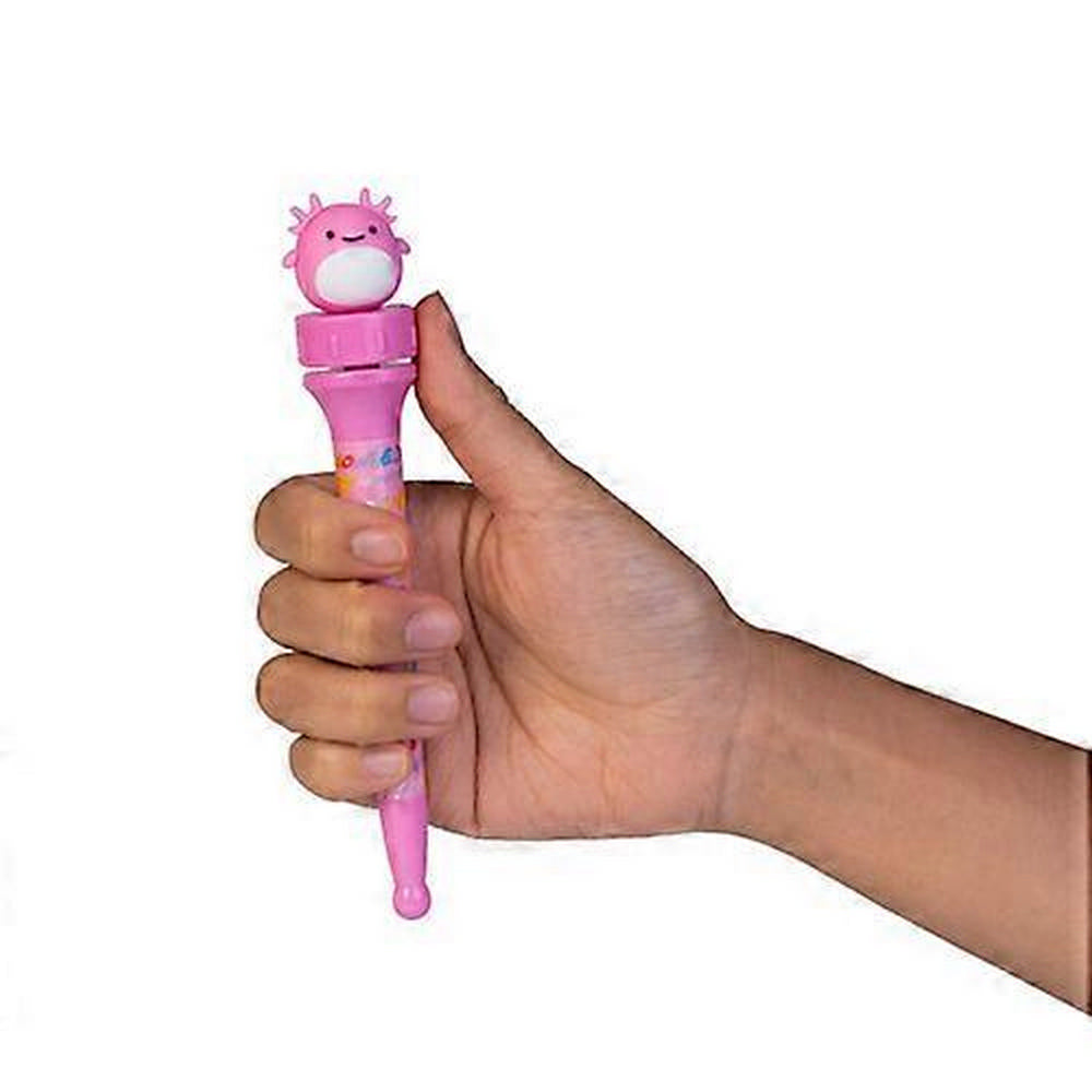 A hand holds a pink novelty pen topped with a cute, smiling pink axolotl