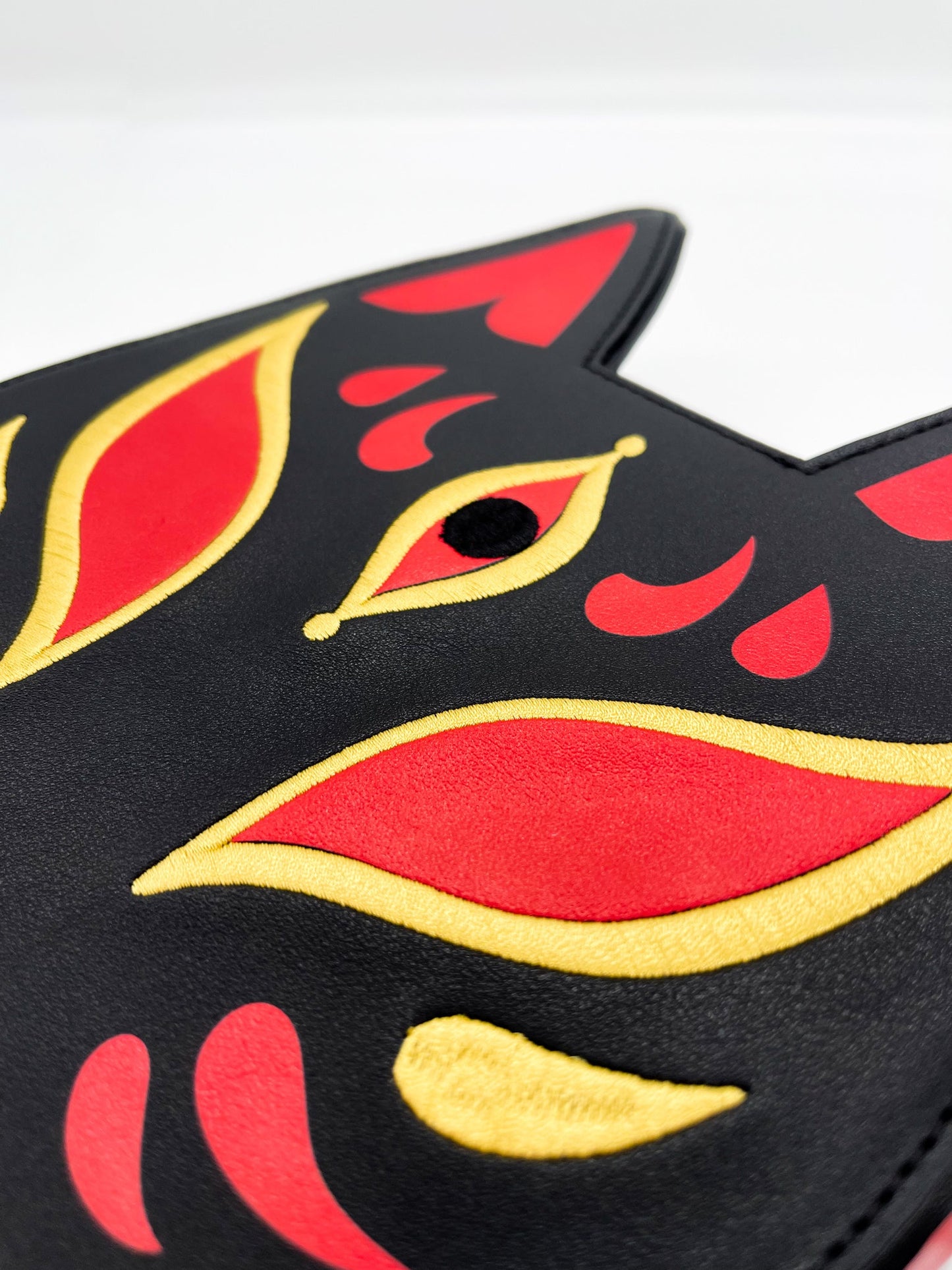Black Kitsune fox mask design with red and gold embroidery, highlighting an eye.
