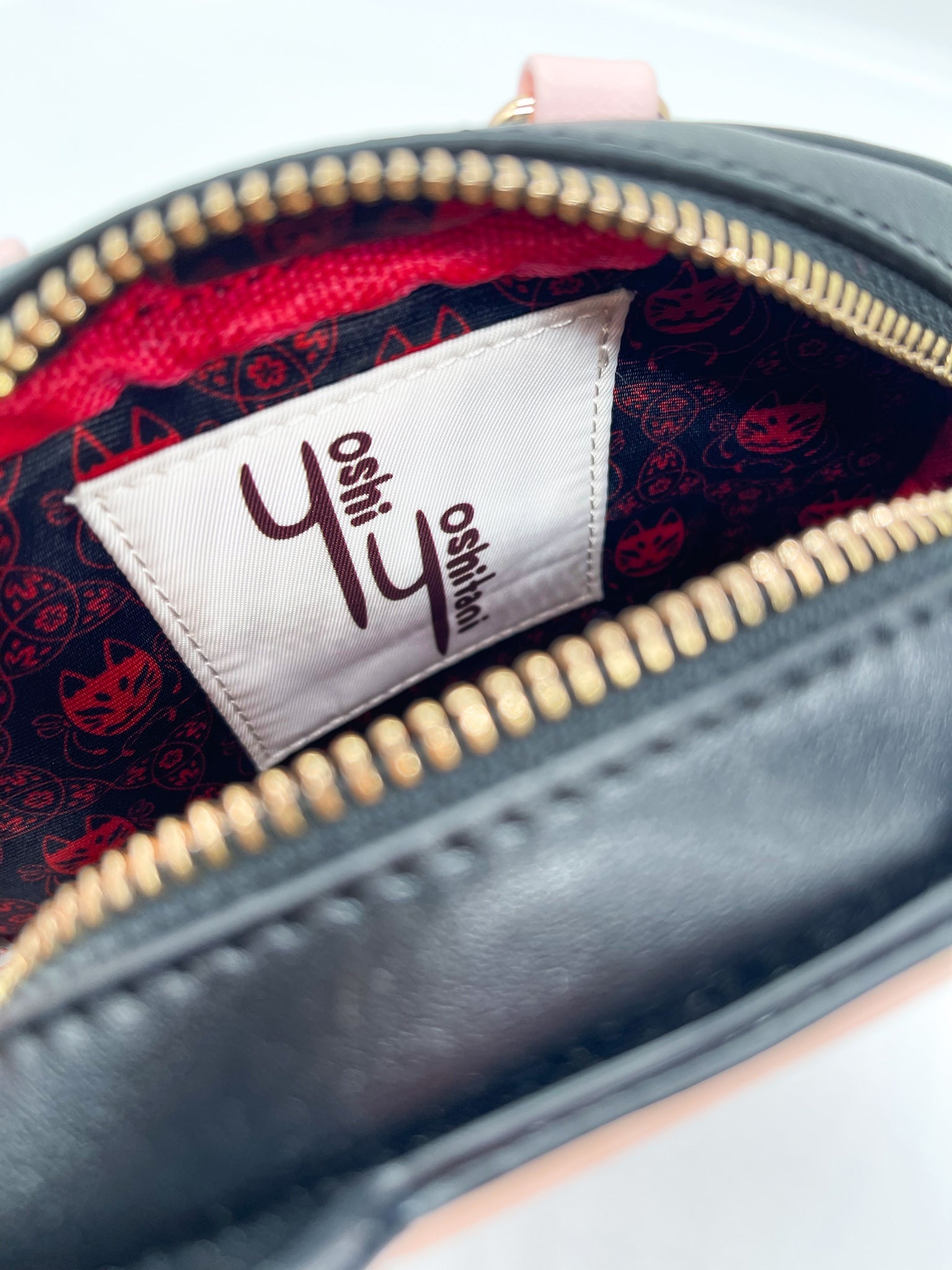 Open black bag's interior: gold zipper, red lining with black cat patterns, and a white 'YY oshi' brand tag.