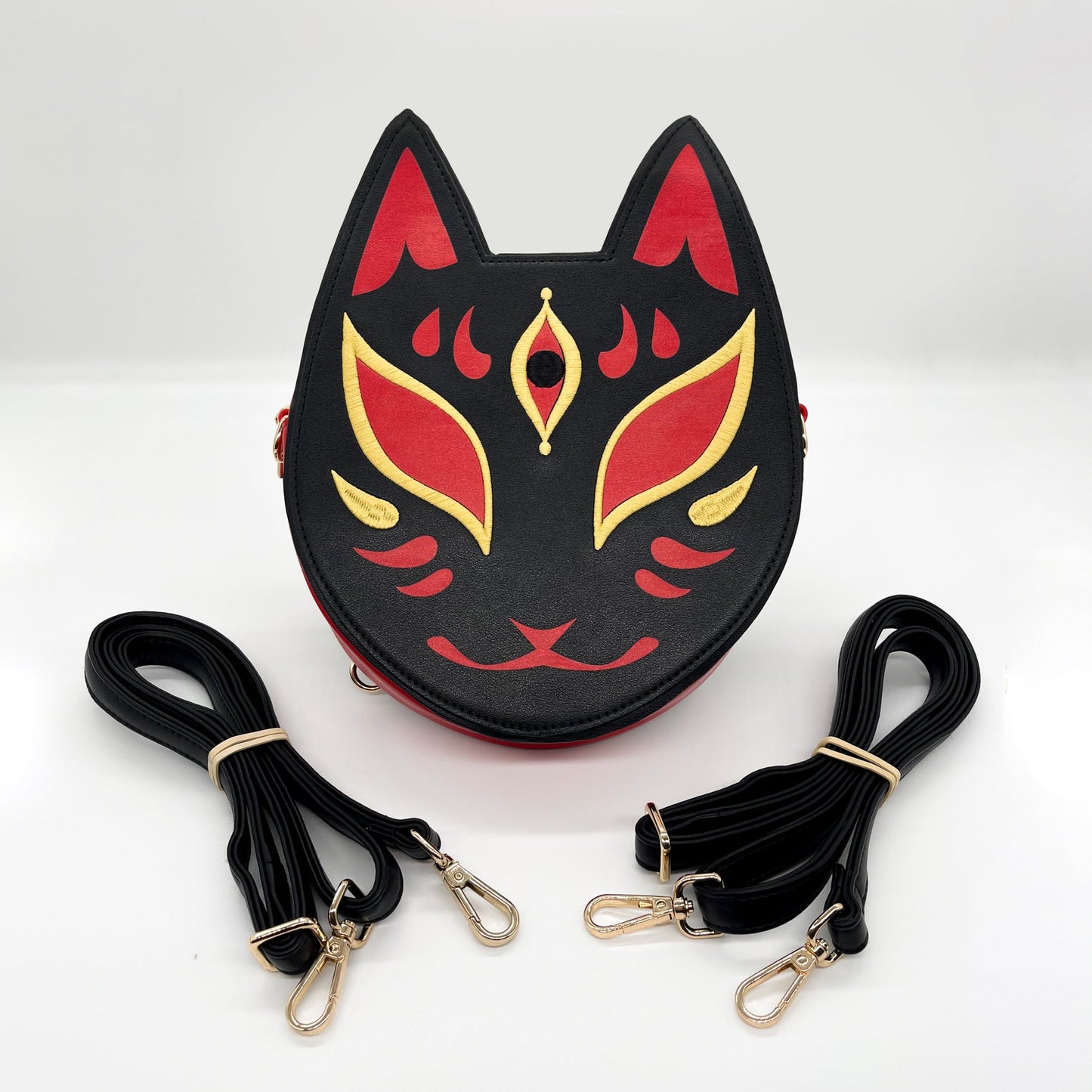 Black, red, and gold Kitsune mask-inspired purse, shown with two coiled black straps.
