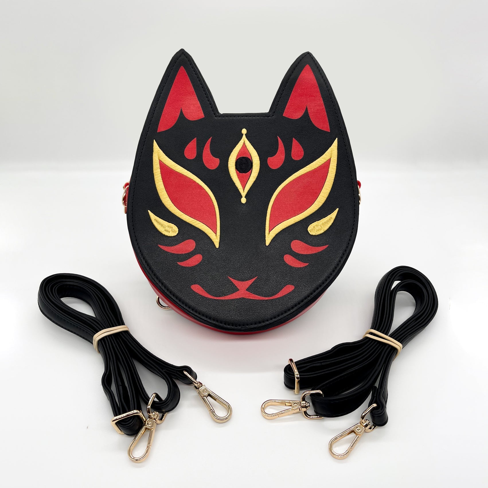 Black, red, and gold Kitsune mask-inspired purse, shown with two coiled black straps.