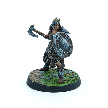Miniature female warrior in fur armor and horned helmet, holding a raised axe and shield, on a grassy base