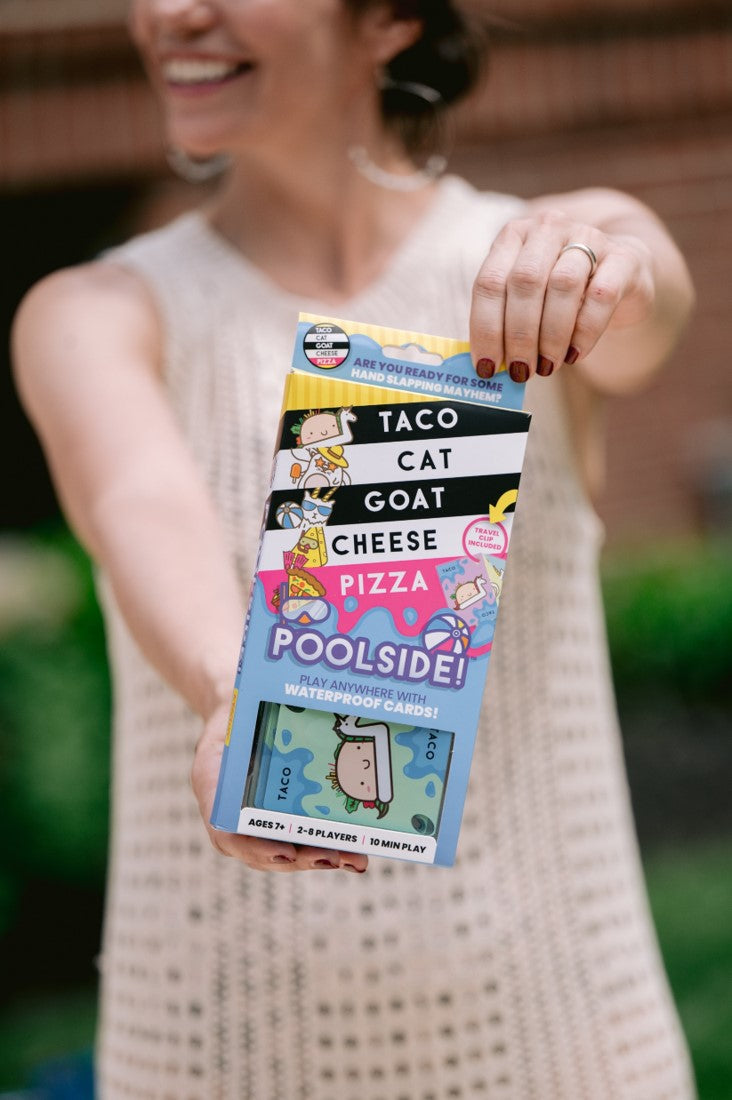 Woman holds up the "Taco Cat Goat Cheese Pizza Poolside!" card game box (waterproof cards)
