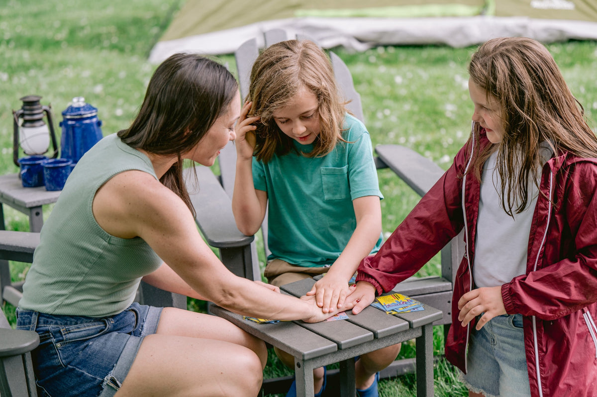 Woman and two children playing a card game outdoors at a camp table, stacking hands on the cards