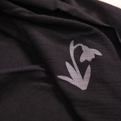 A light grey stylized snowdrop flower graphic printed on dark, textured fabric hooded cloak