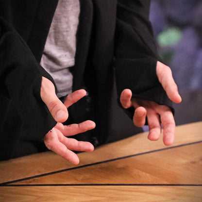 Two hands in black sleeves with thumbholes are open and gesturing above a wooden table