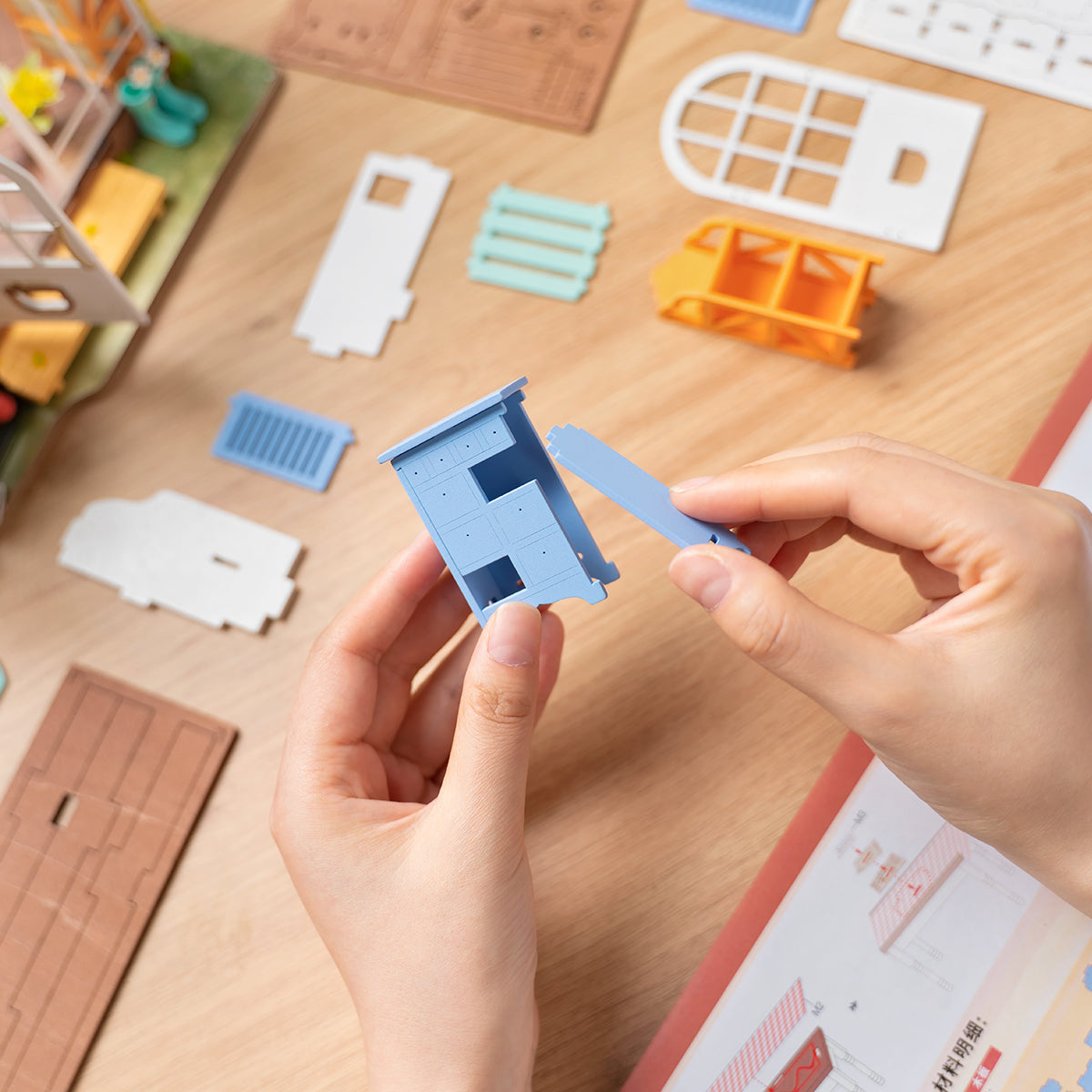Hands assembling a small blue miniature cabinet from a dollhouse construction kit