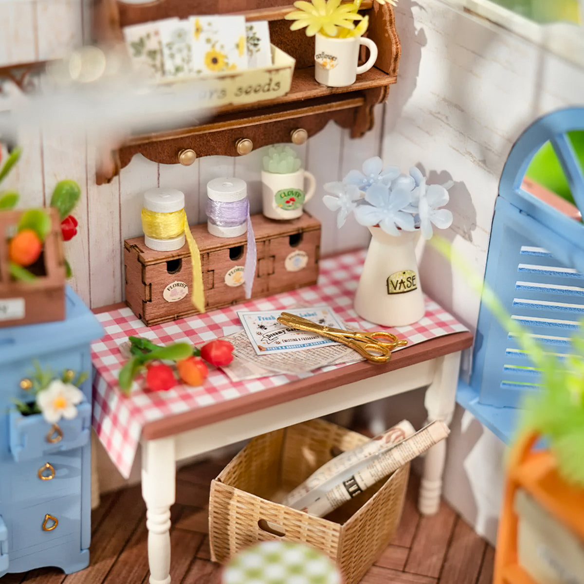 Detailed miniature craft room scene featuring a table with a vase, golden scissors, and thread spools