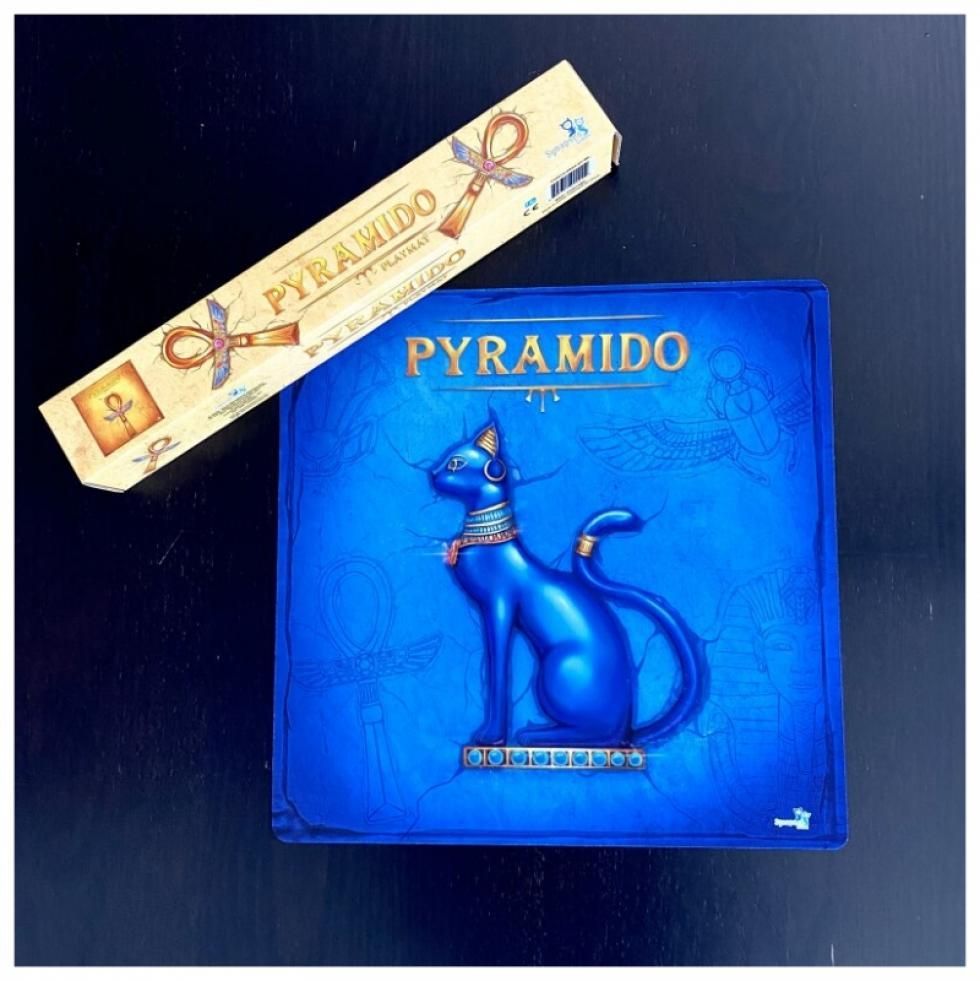 Blue Pyramido game box featuring a raised Egyptian cat, next to a Pyramido playmat tube.