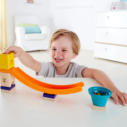 Smiling child playing with an orange marble run construction set