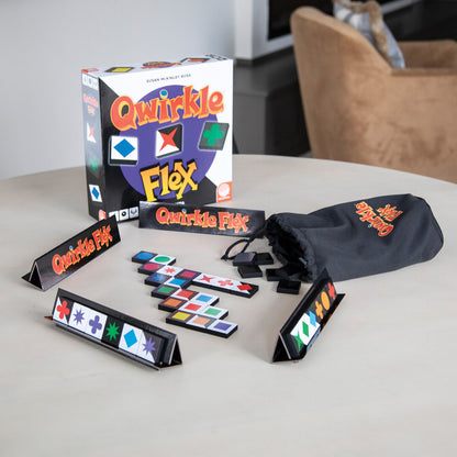 Qwirkle Flex board game components on a table: box, colorful geometric tiles, tile racks, and a black drawstring bag