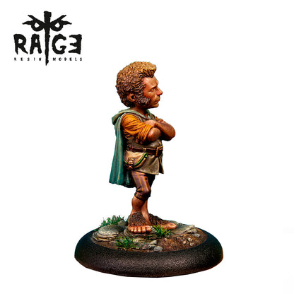 A painted miniature Yarry Light Feet figure, a short man with curly hair, bare hairy feet, and a green cloak, standing with crossed arms on a rocky base