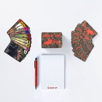 A Rack UP The Hunting Card Game set is displayed with two fanned card decks, a game box, a white score pad with grid lines, and an orange pen on a plain background