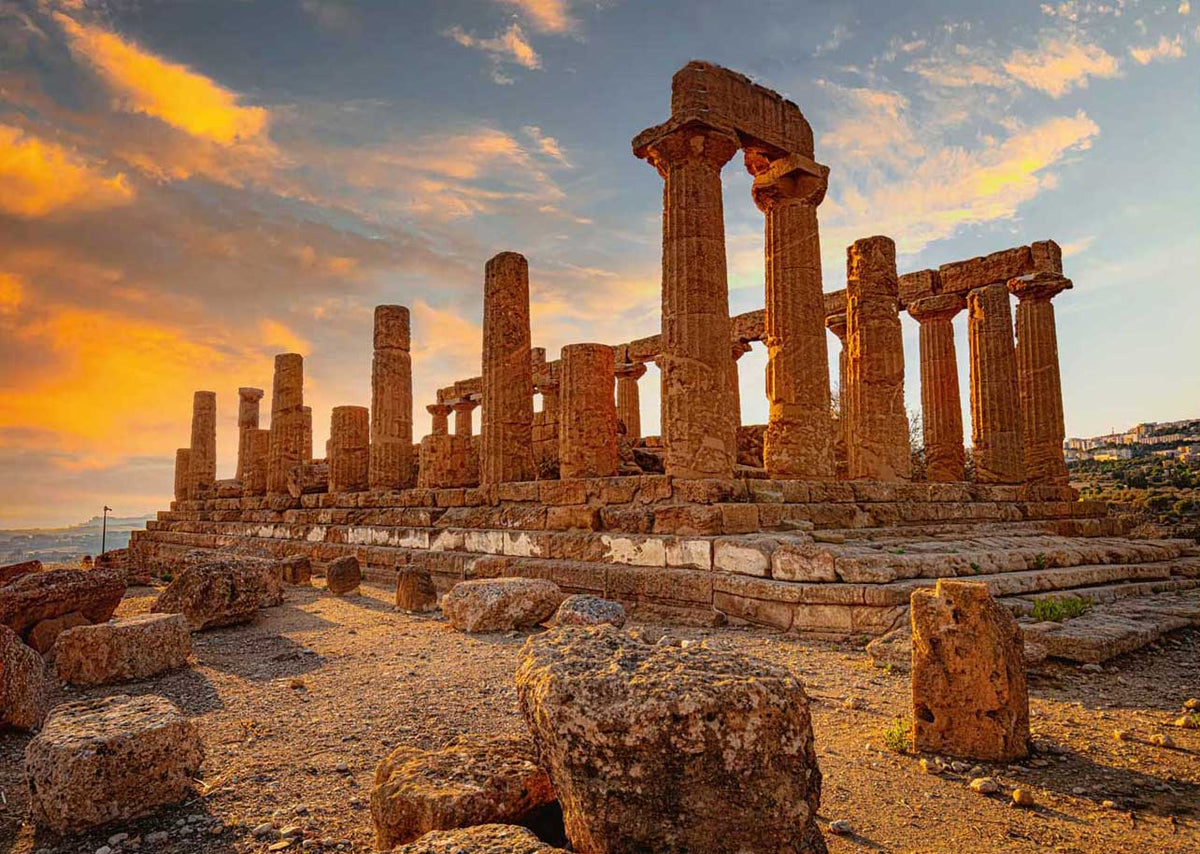 Ancient Greek temple ruins at sunset with towering stone columns and a dramatic orange sky