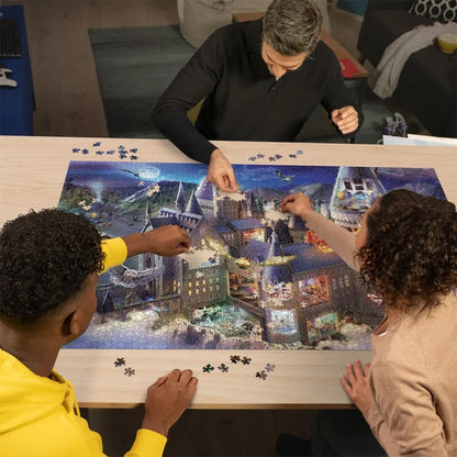 Three people assemble a large Hogwarts castle jigsaw puzzle at night on a wooden table