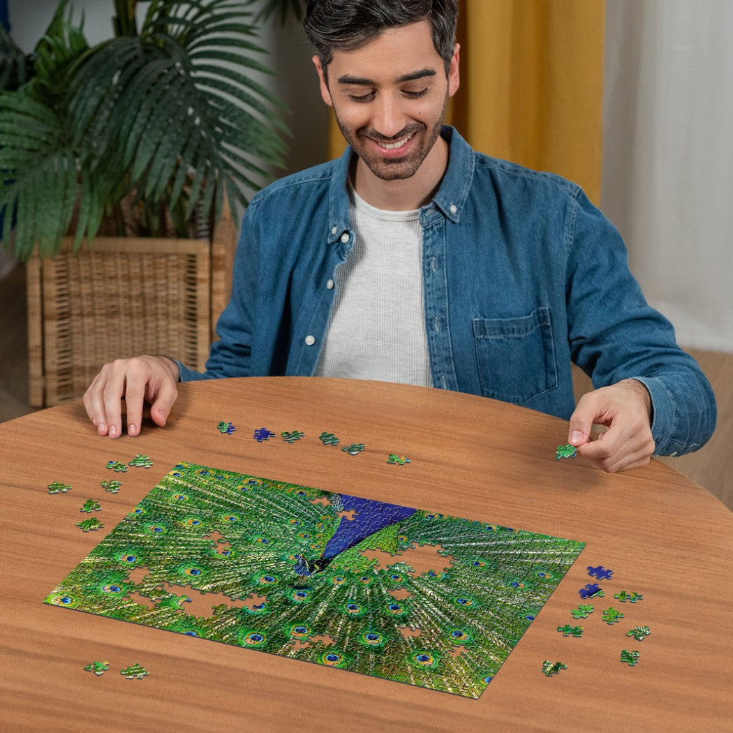 Smiling man in denim shirt assembling a colorful peacock jigsaw puzzle on a wooden table