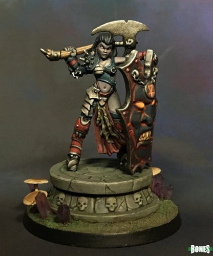 Painted miniature of a fierce female warrior, axe raised, wielding a demonic shield with glowing eyes on a skull pedestal.